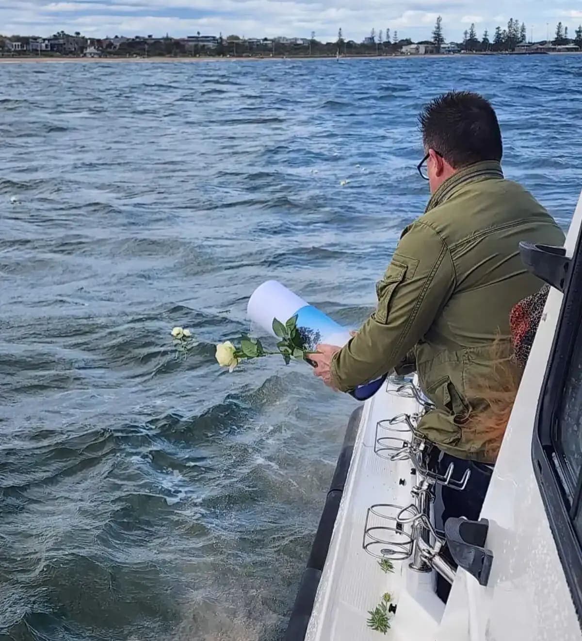 A man holding flowers at the side of the boat, looking out over the water