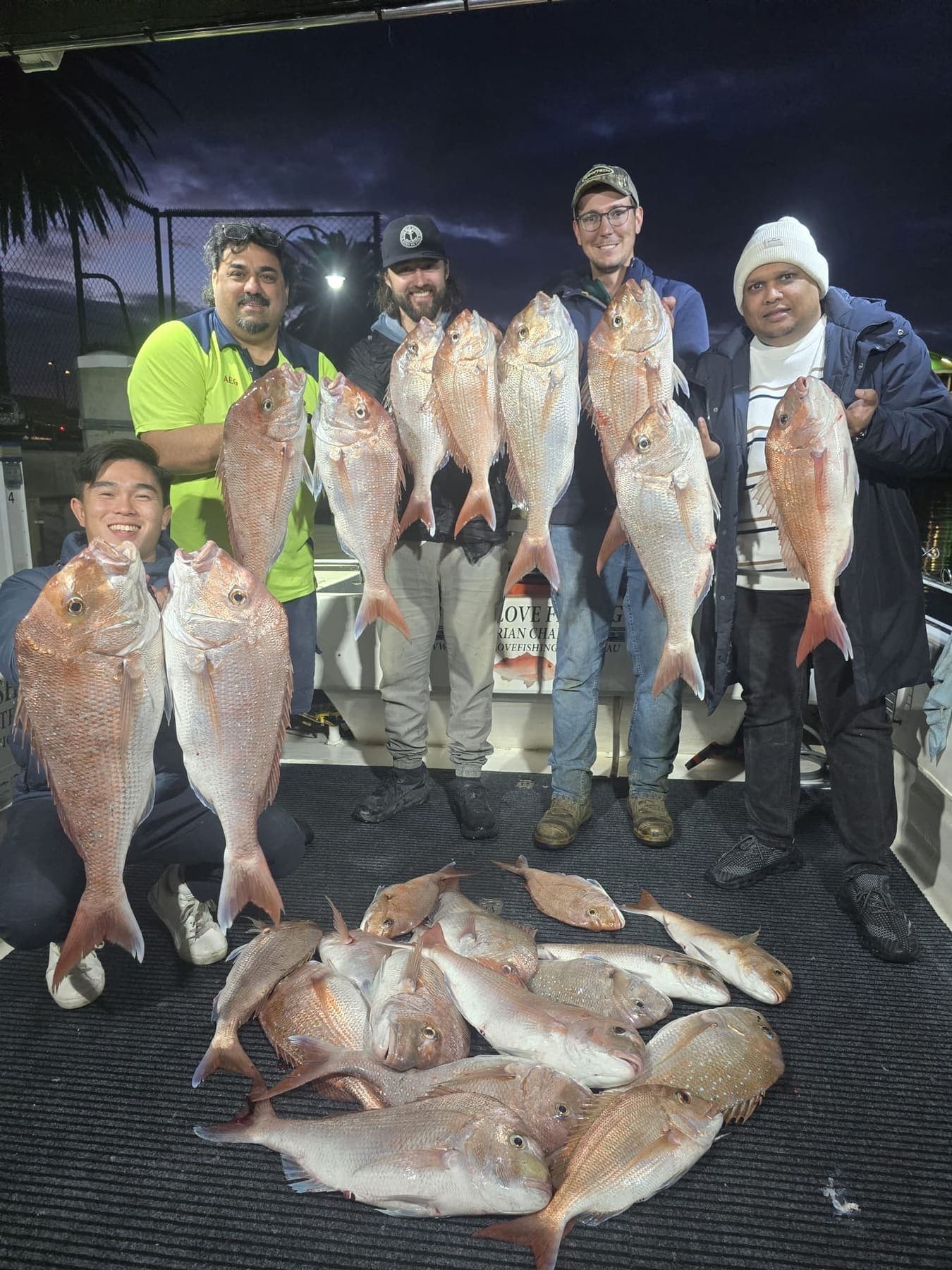 Five guests holding up snapper on the back deck at dusk, with more of the catch on the deck in front