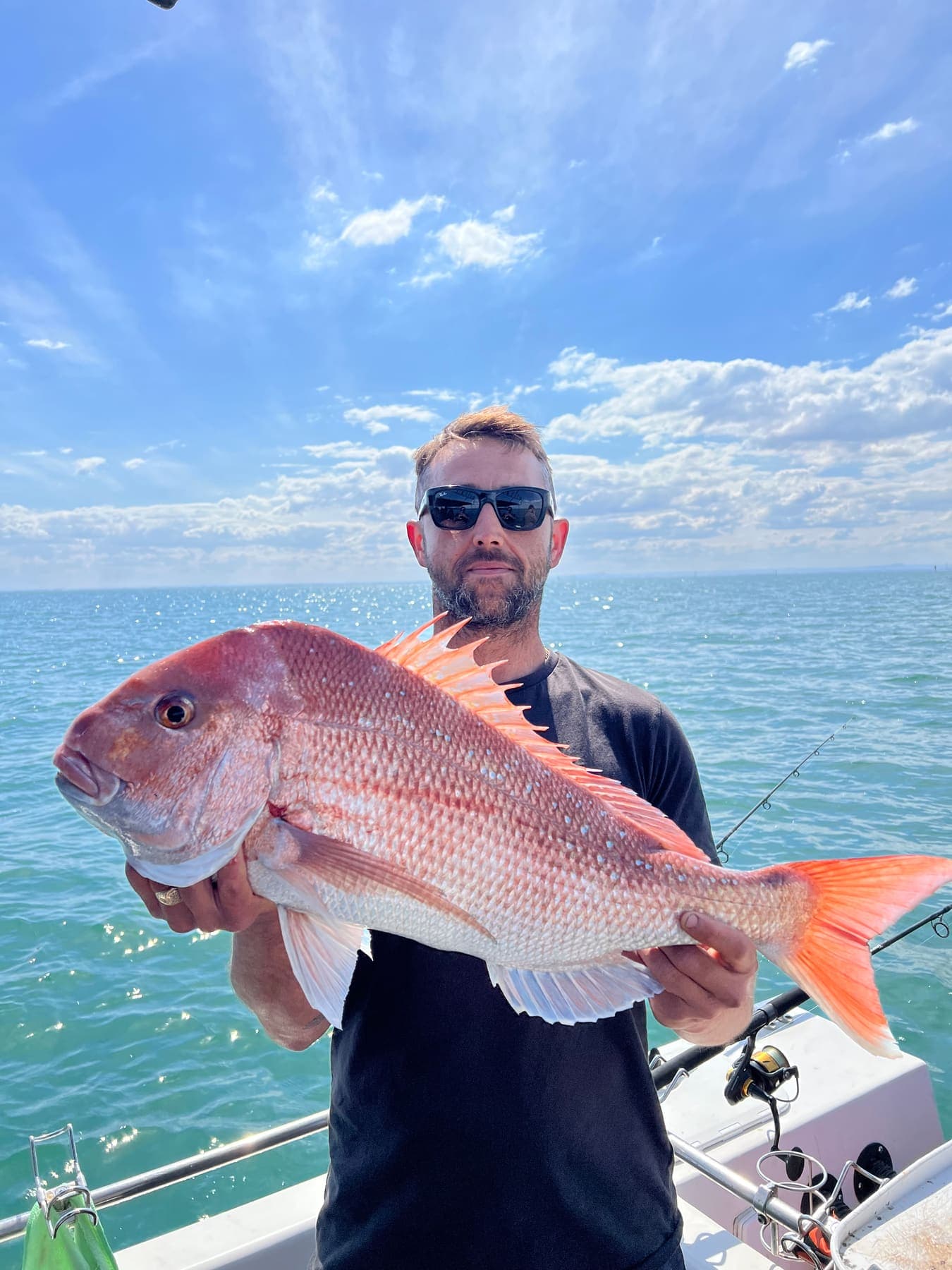 A guest in sunglasses holding a big snapper out on the bay under a blue sky