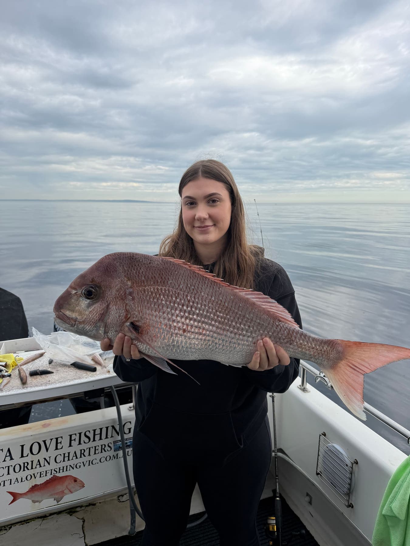 A guest holding a large snapper on the boat with glassy calm water behind her