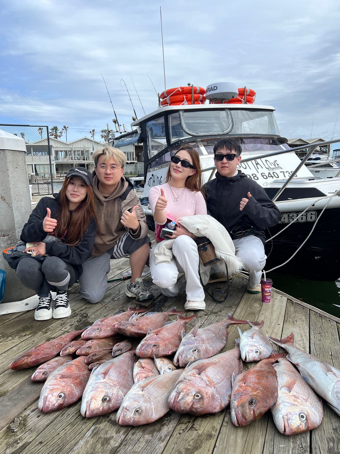 Four guests giving thumbs up on the dock beside the Gotta Love Fishing boat, with a row of snapper in front
