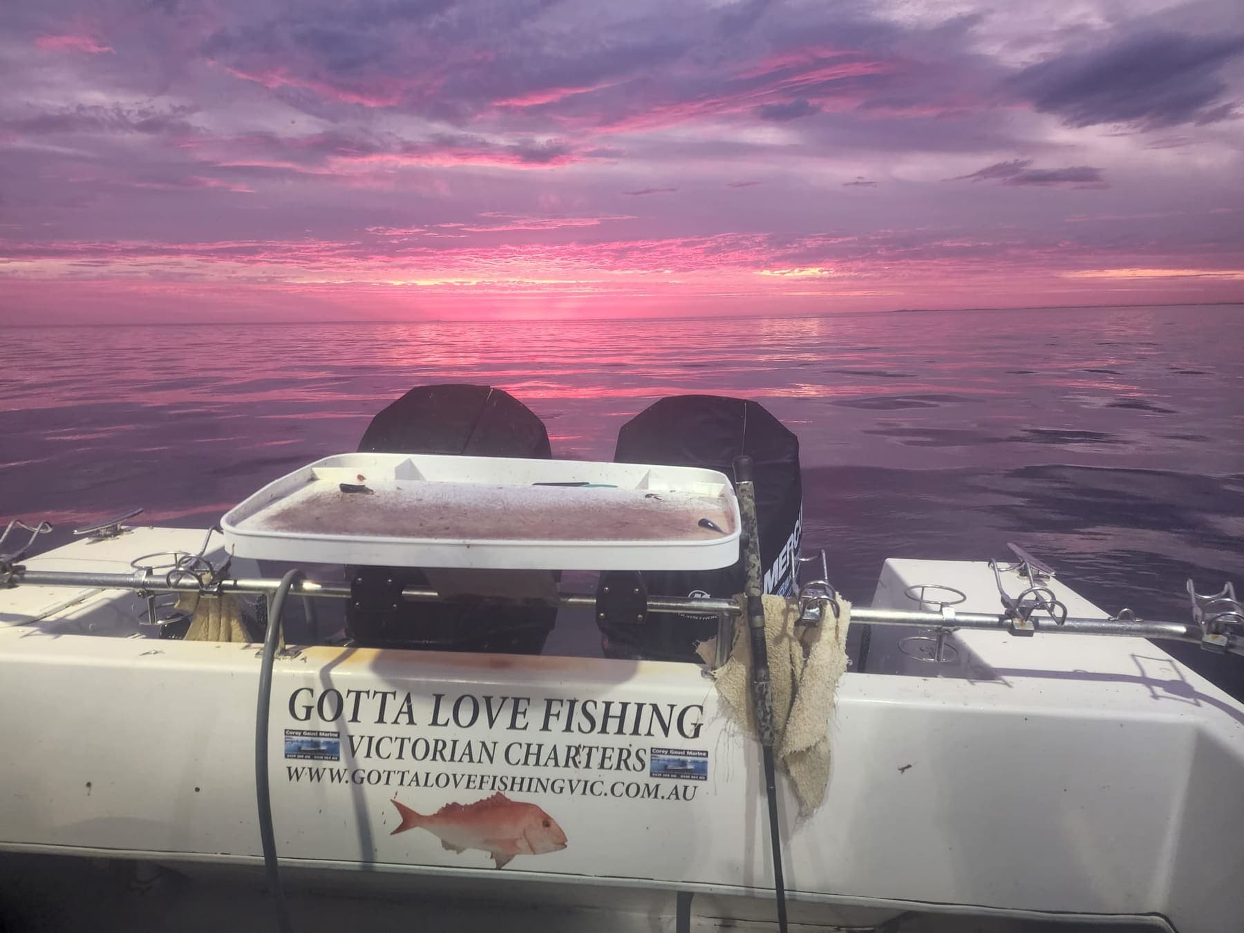 Pink and purple sunset over the water seen from the stern of the boat