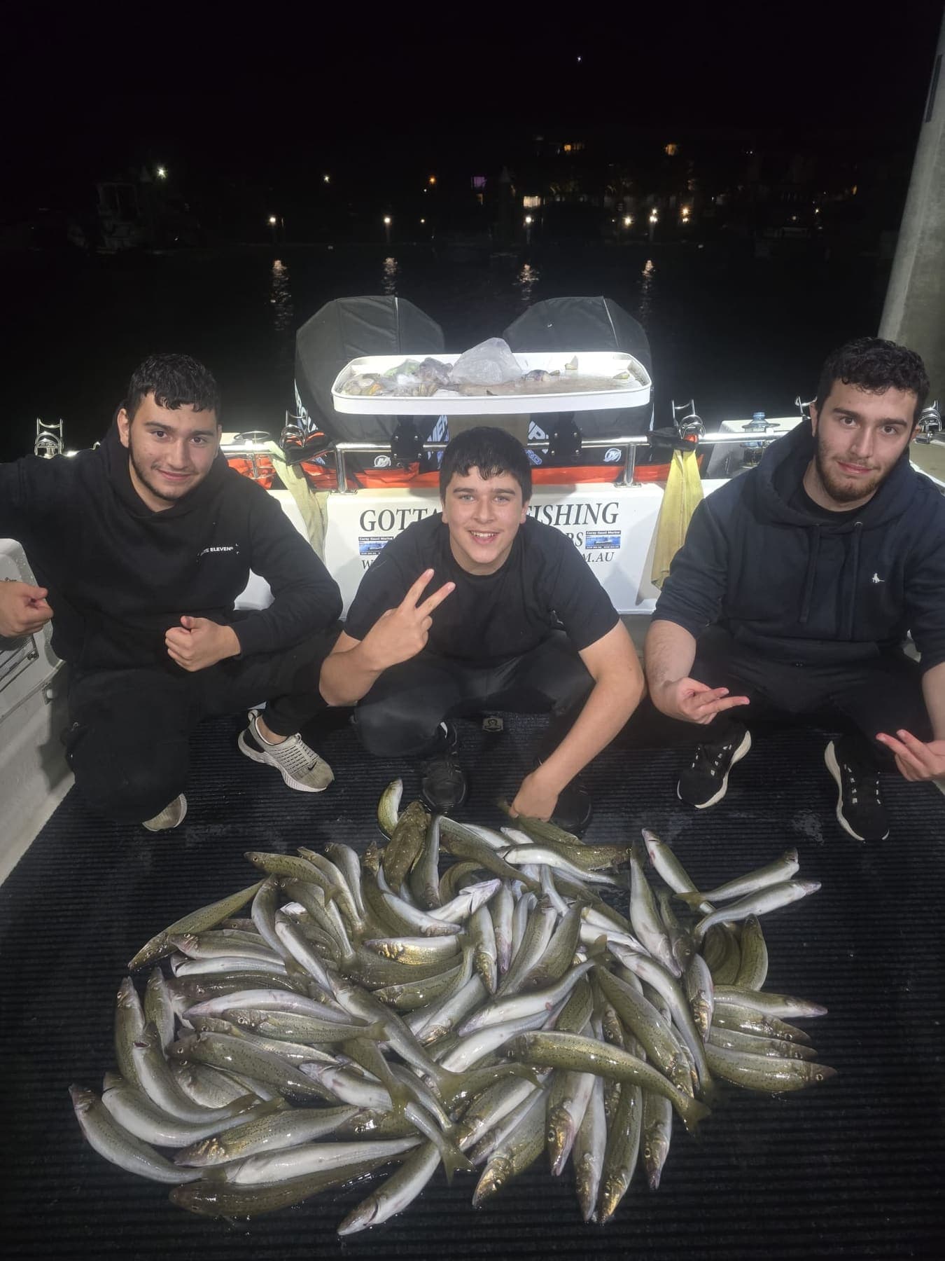 Three young guests crouched behind a big pile of whiting on the deck at night