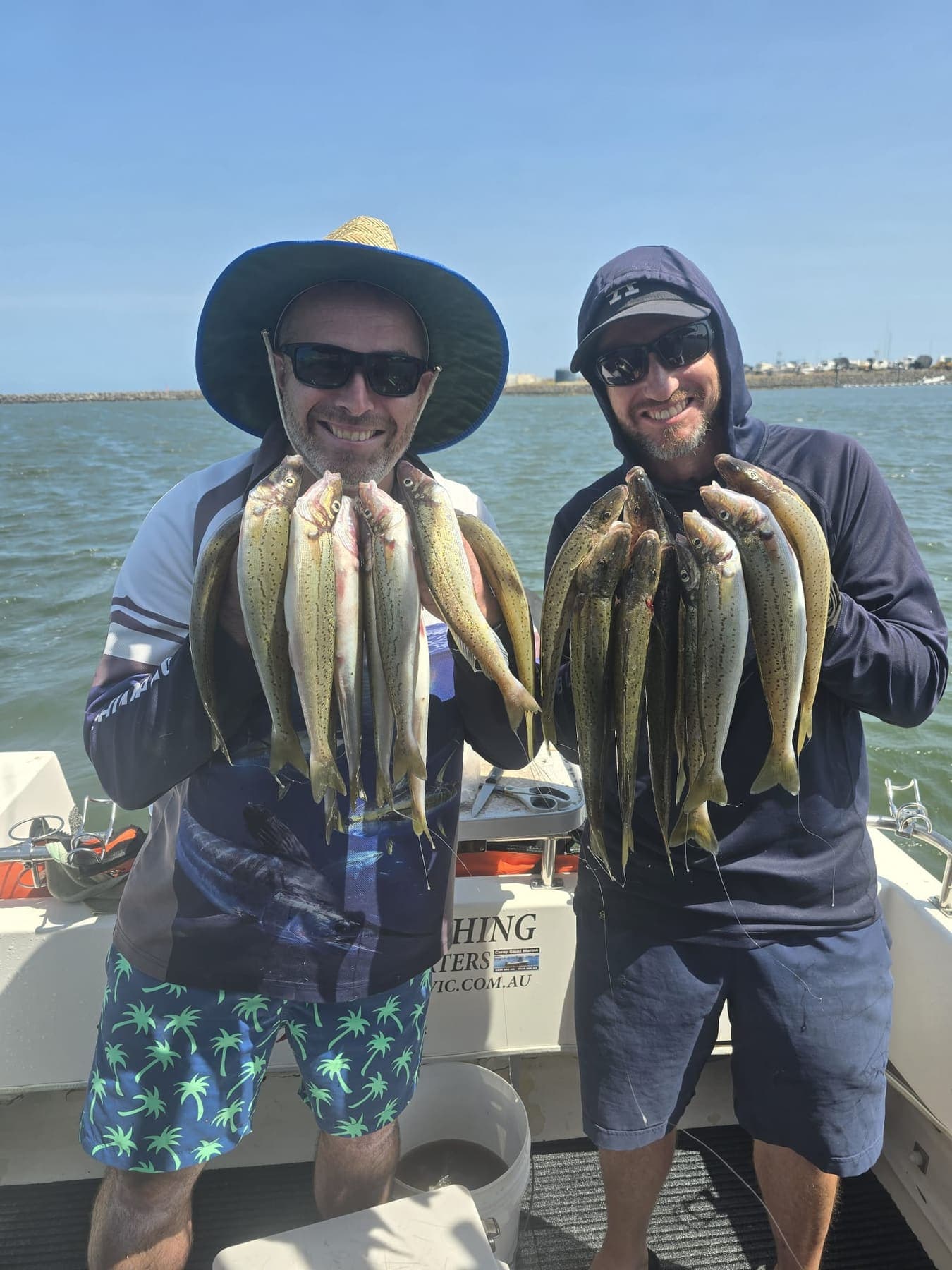 Two guests in sunglasses holding up bunches of King George whiting on the bay