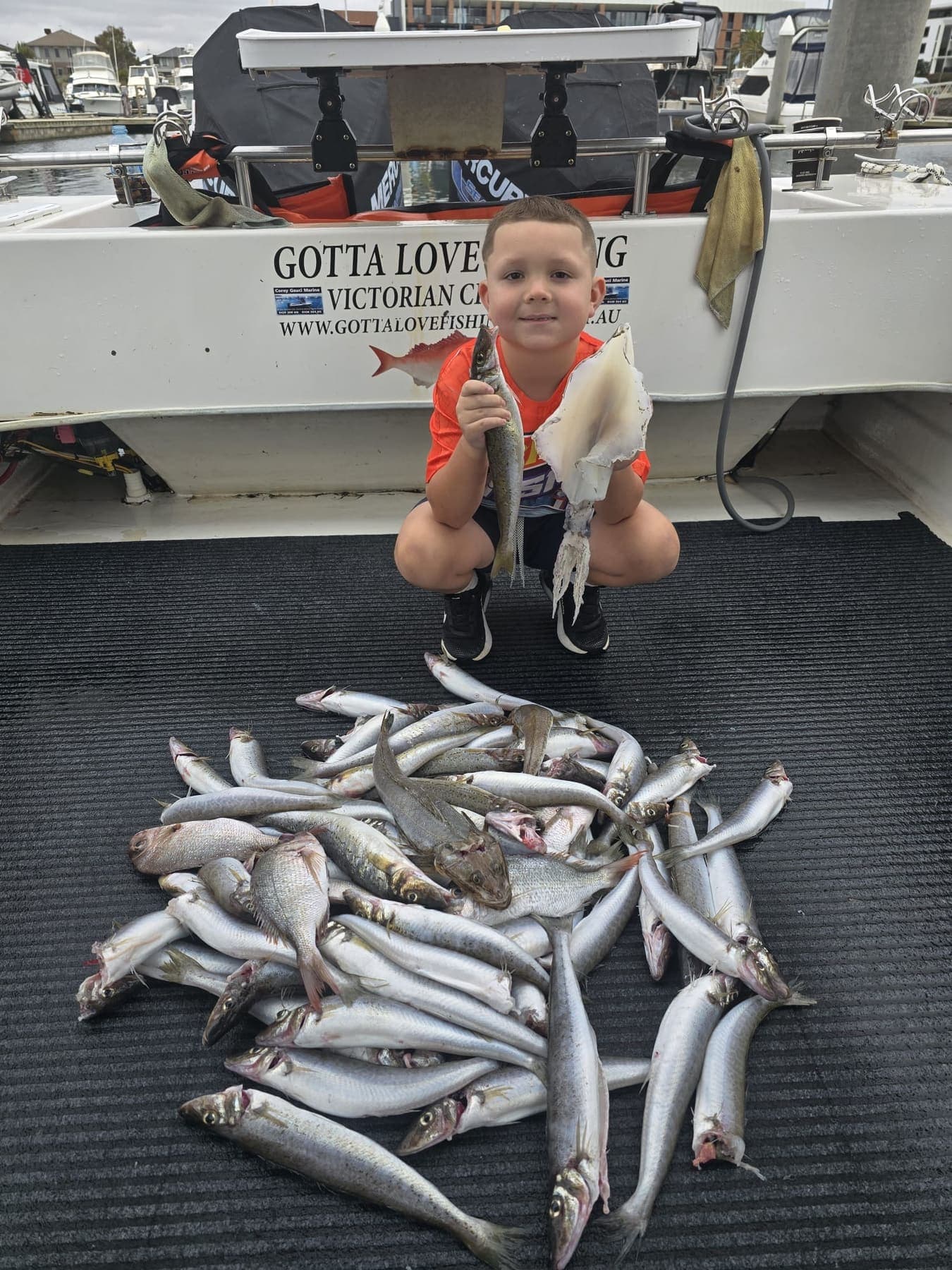 A young boy holding a whiting and a calamari behind a mixed catch of whiting, flathead and pinkies